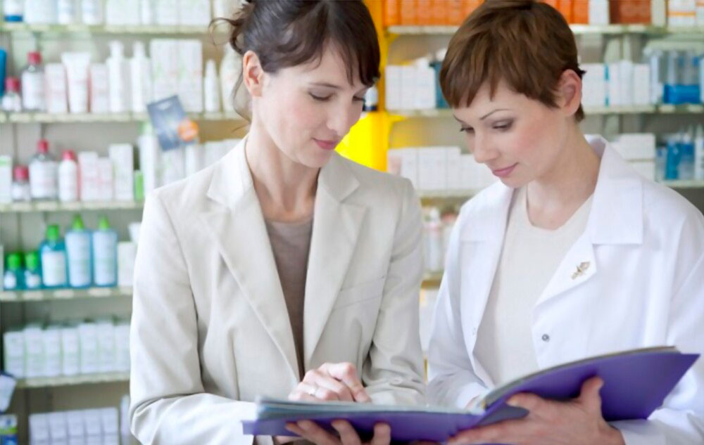 Dos farmacéuticas en una farmacia consultando una carpeta con documentos